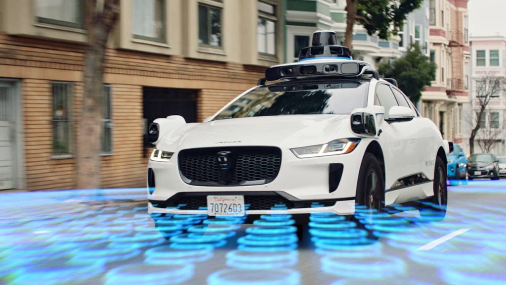 A white Waymo Jaguar driving through a San Francisco street.